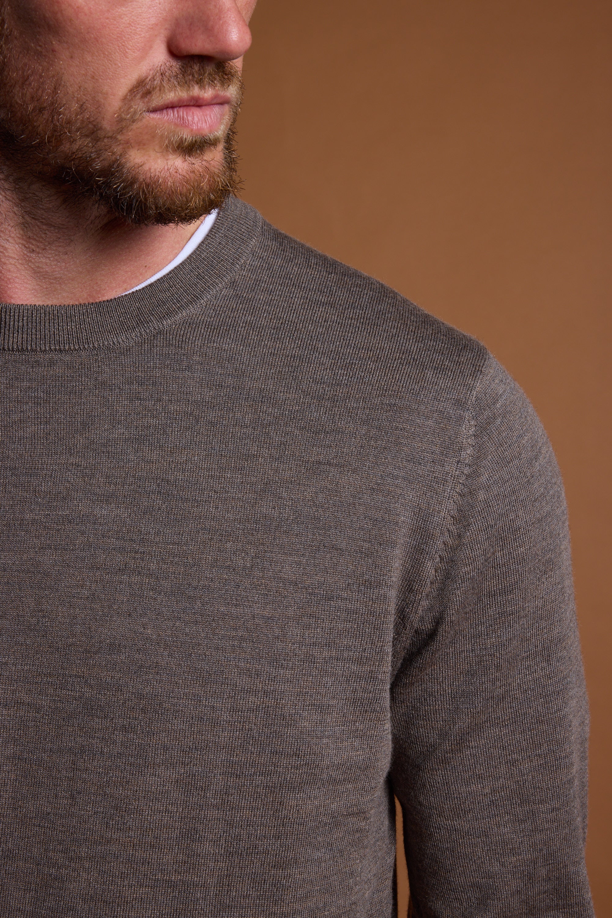 A close-up of a bearded man wearing the Barkers Skyland ZQrx Merino Crew over a white shirt, set against a plain brown background. Only the lower part of his face and neck are visible.