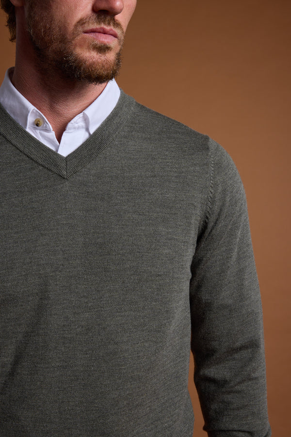 A man is shown from shoulders to chest wearing the Barkers Skyland ZQrx Merino Vee, a grey ethically sourced New Zealand merino wool V-neck sweater over a white button-up shirt, against a brown background. His face is partially visible with a short beard and mustache.