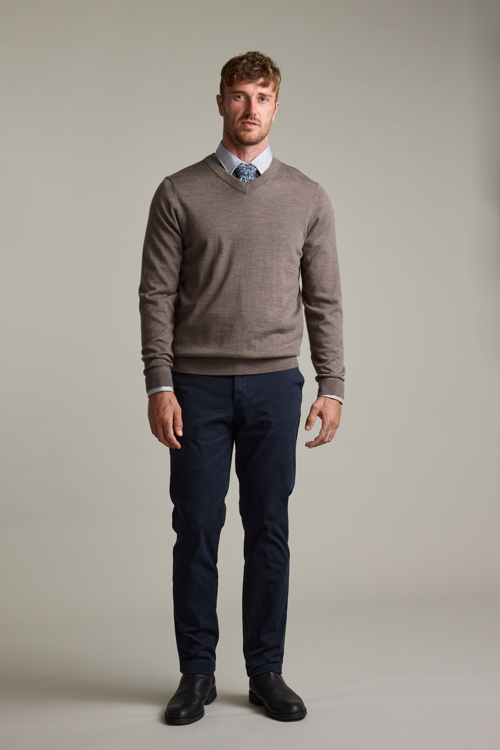 Man wearing Barkers Skyland ZQrx Merino Vee sweater, blue shirt, tie, dark pants, black shoes indoors.