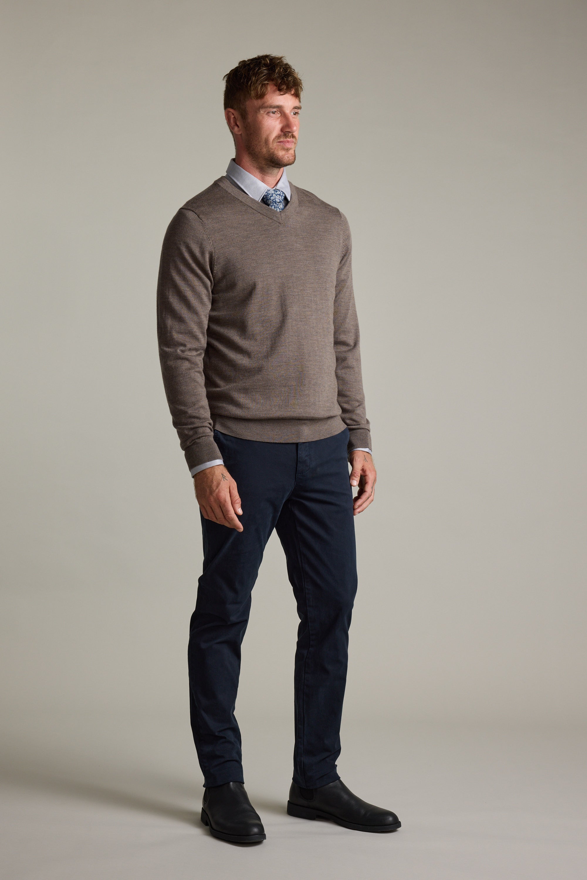 Man wears Barkers Skyland ZQrx Merino Vee sweater with blue shirt, tie, pants, and black shoes.