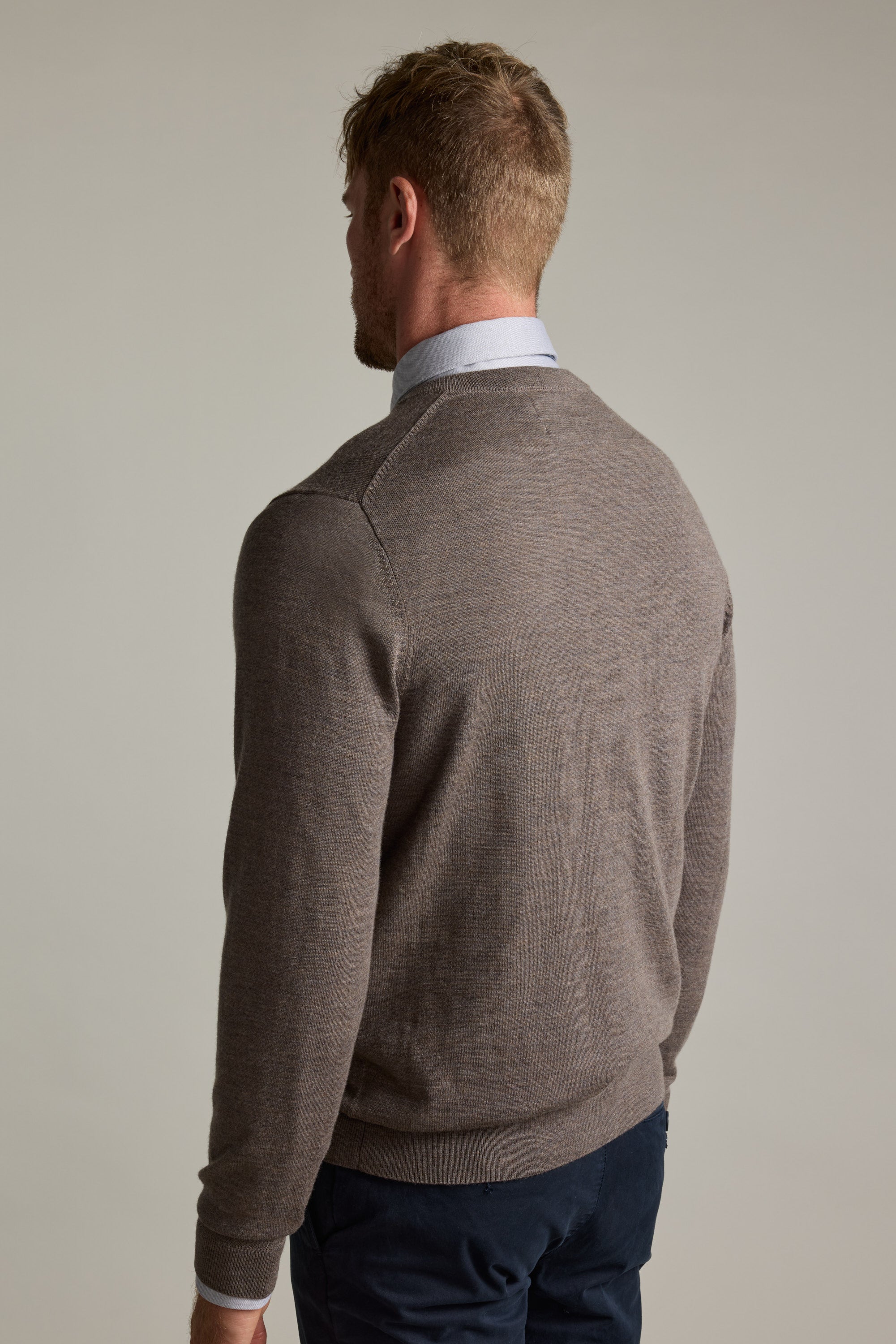 Man in a brown Barkers Skyland ZQrx Merino Vee sweater and blue pants stands, back to camera.