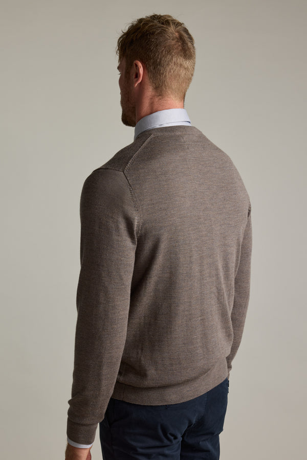 Man in a brown Barkers Skyland ZQrx Merino Vee sweater and blue pants stands, back to camera.