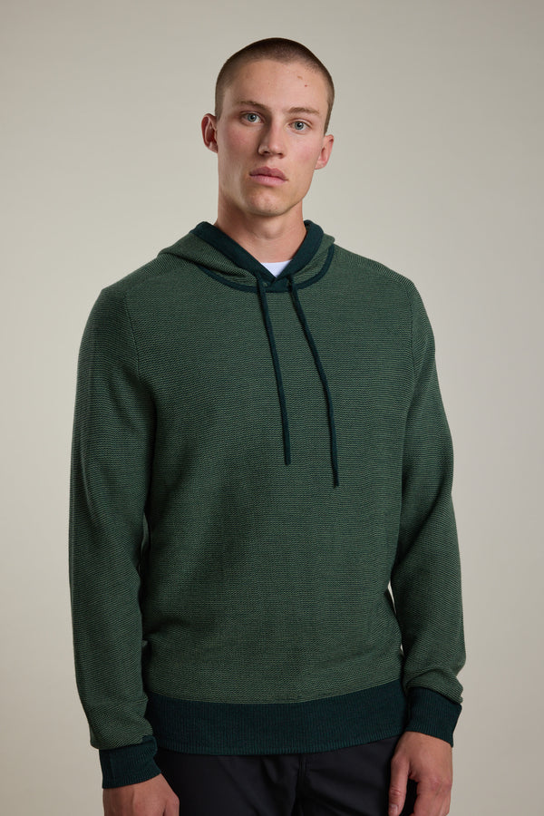 A young man with short hair wears the Barkers Roxbury Merino Hoody, featuring a front pocket and drawstrings, standing against a plain light background and looking directly at the camera with a neutral expression.