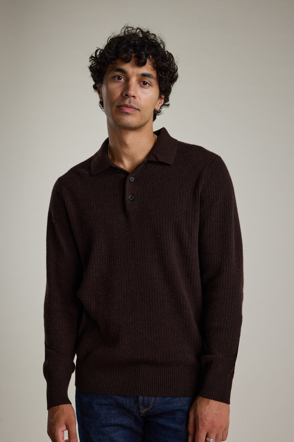 A man with curly dark hair wears the Barkers Braxton Merino Long Sleeve Polo, featuring ribbed detailing and buttons, standing against a plain light background.