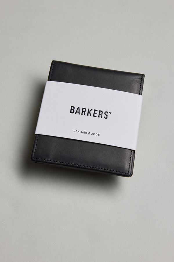 A black Harris Leather Fold Wallet by Barkers, wrapped in a white paper band with the brand name, is placed on a light gray surface.