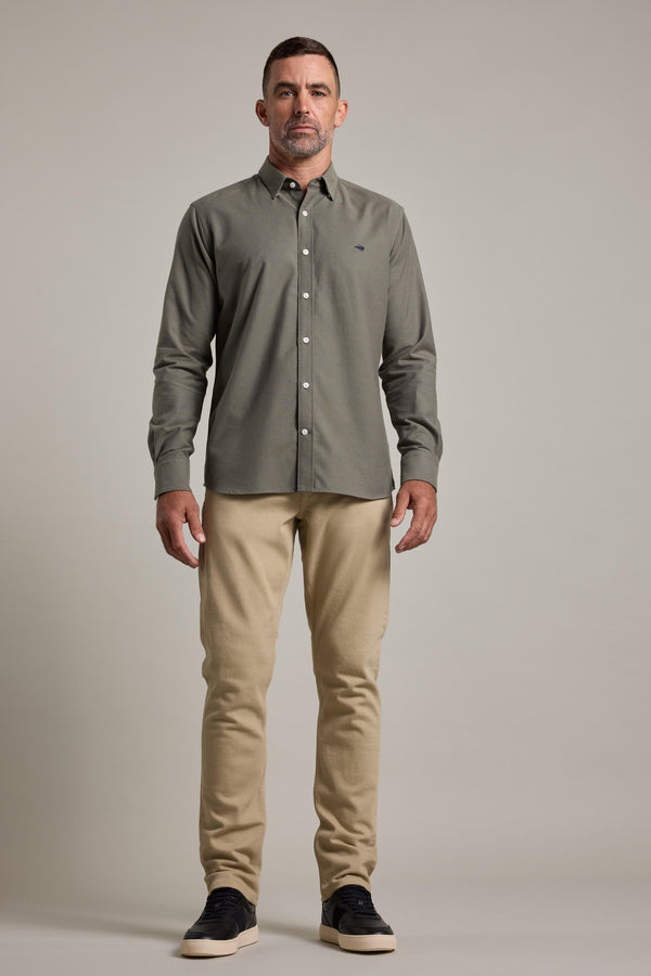 A man faces forward wearing a Barkers Maynard Oxford Shirt in olive green, beige pants, and black sneakers with white soles against a plain light gray background.