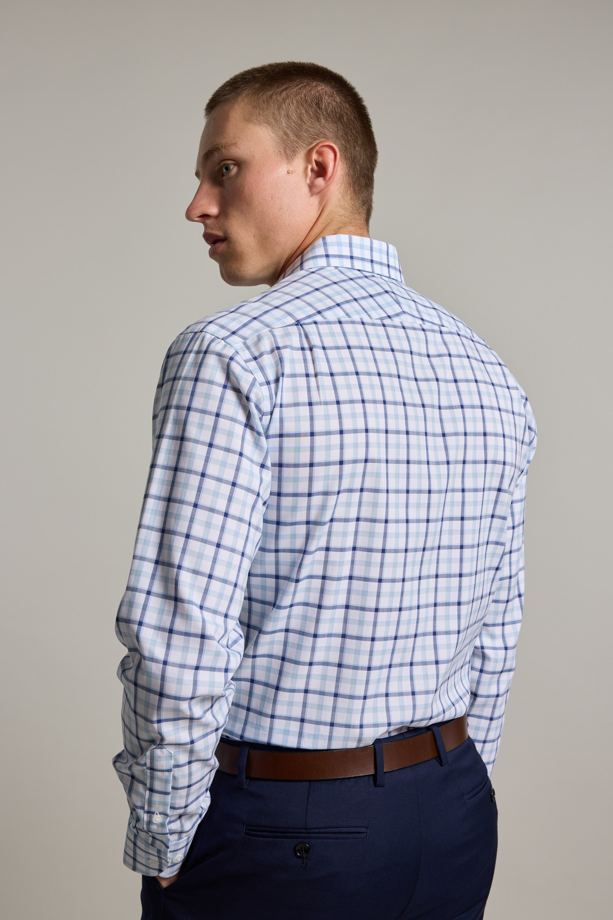 A man with short hair, wearing the Barkers Wesley Check Business Shirt and navy pants, stands turned slightly to the side, looking over his shoulder against a plain background.
