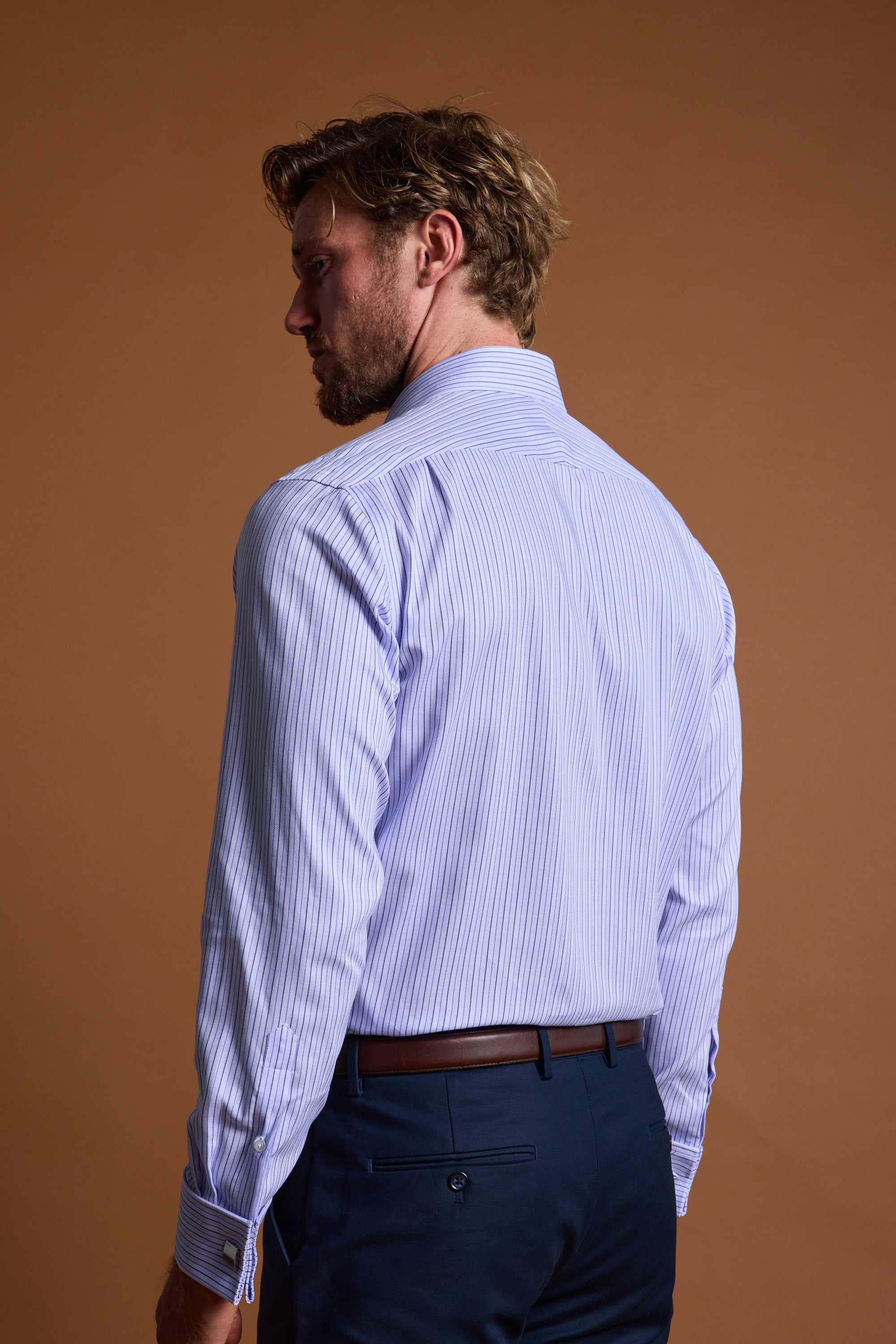 A man with light brown hair, seen from behind, wears the Barkers Asmara French Cuff Business Shirt and dark blue trousers, standing against a plain brown background.