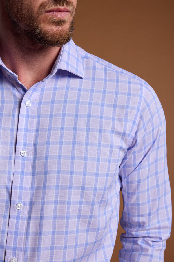 A man wearing the Barkers Larry Check Business Shirt, featuring a light purple and white plaid design with a tailored fit, is shown from shoulders to mid-torso against a brown background. His beard and mustache are partially visible.