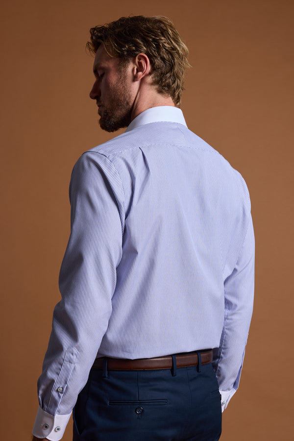 A man with light brown hair and a beard, seen from behind, wears the Barkers Felix Stripe Business Shirt in tailored fit with white collar and cuffs, navy trousers, and a brown belt—Eco Easy Care—set against a brown background.