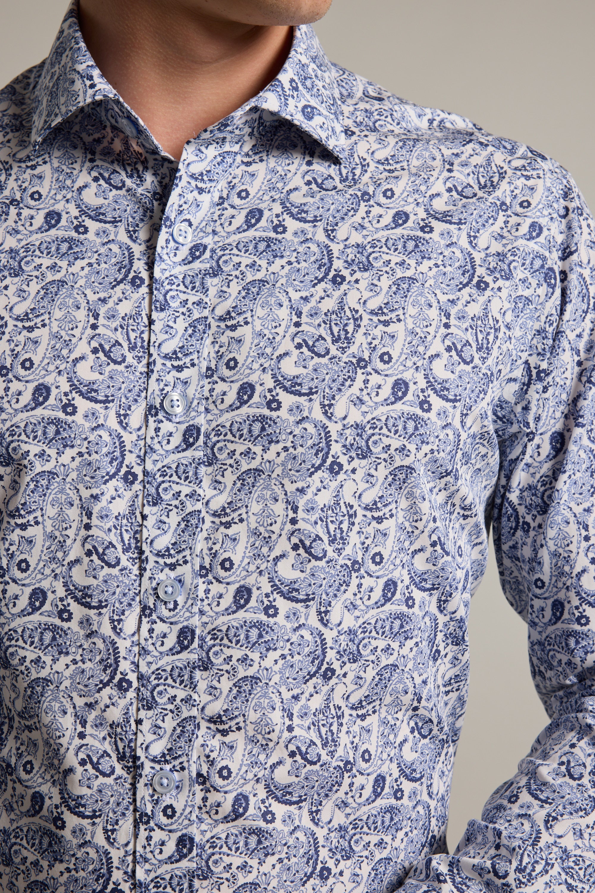 A person wears the Buckman Print Business Shirt by Barkers, a tailored, long-sleeved button-up featuring a blue paisley pattern on white—an ideal choice for adding style and sophistication to any professional wardrobe.