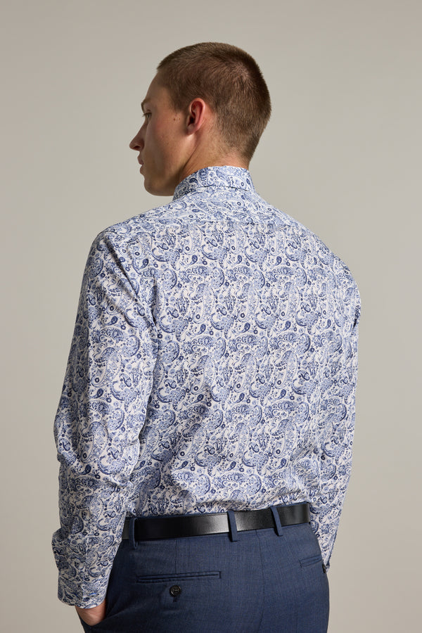 A man with short hair, seen from behind, wears the Barkers Buckman Print Business Shirt with a blue and white paisley pattern, paired with dark blue trousers and a black belt, standing against a plain light background.