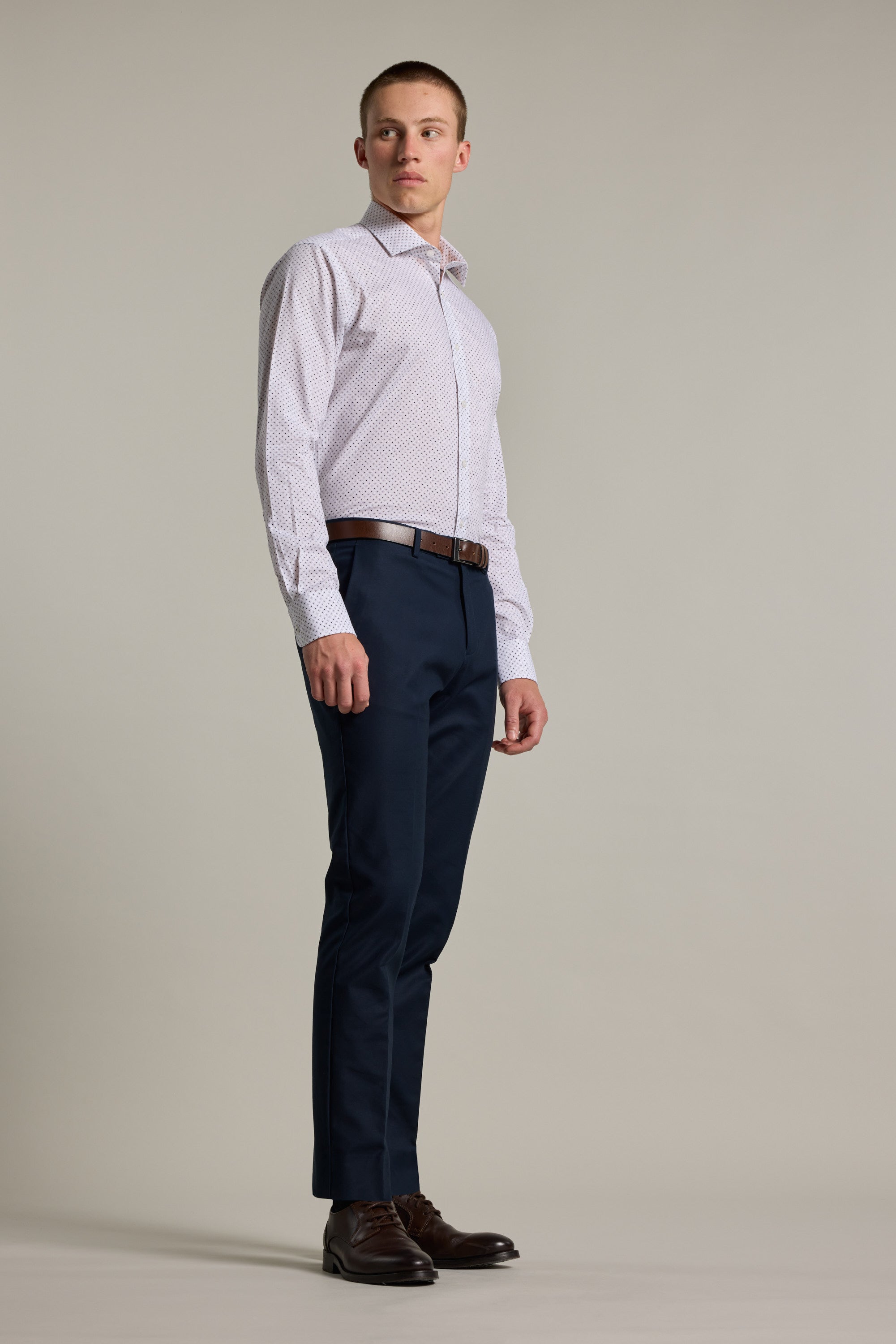 A man wears the Barkers Foster Print Business Shirt, styled with dark blue trousers, a brown belt, and brown dress shoes, standing against a plain background and looking slightly to his left.
