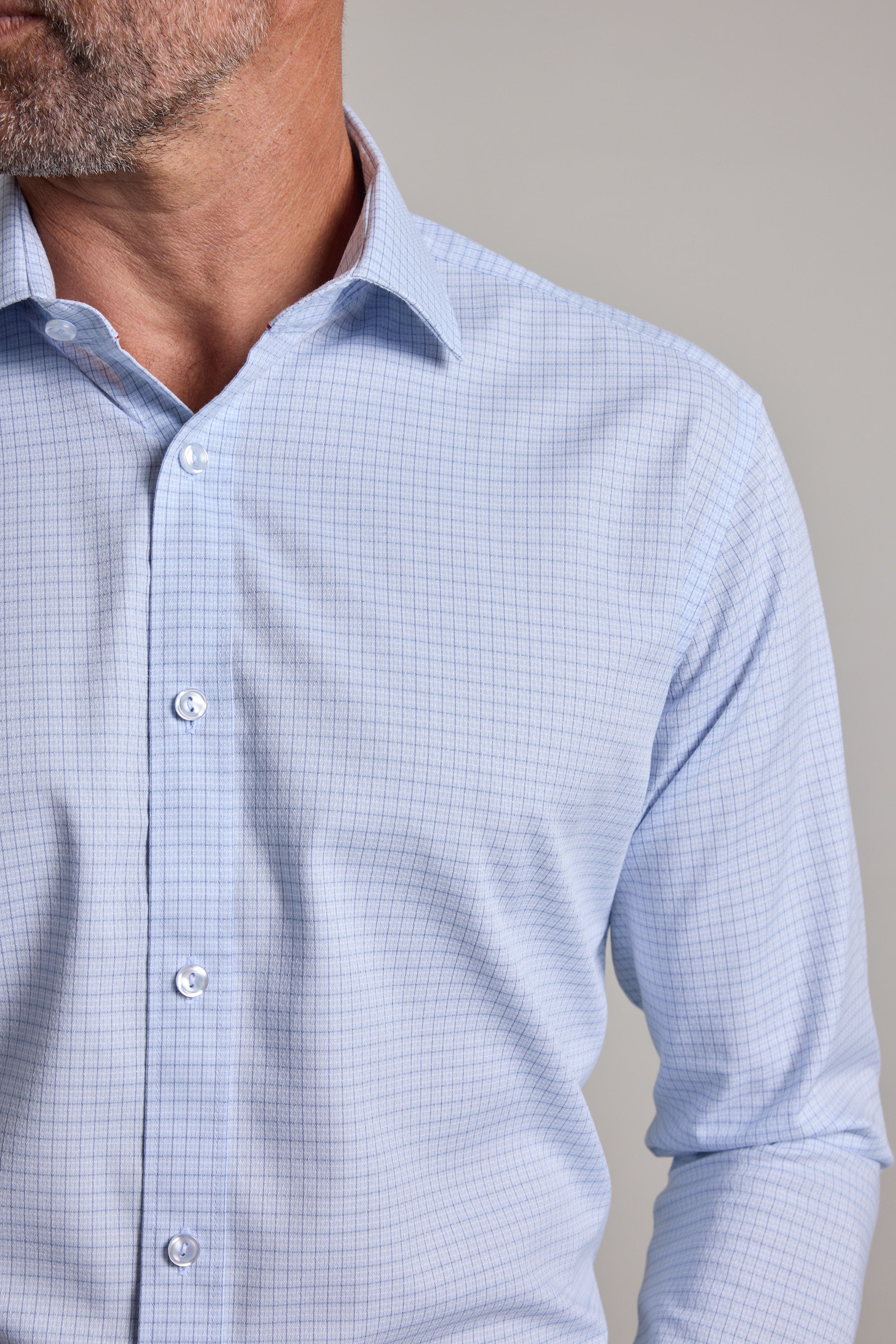 A close-up of a man wearing the Barkers Hunter Check Business Shirt, a light blue, long-sleeve, wrinkle-free shirt with a small checkered pattern. Only his lower face, neck, and upper torso are visible.