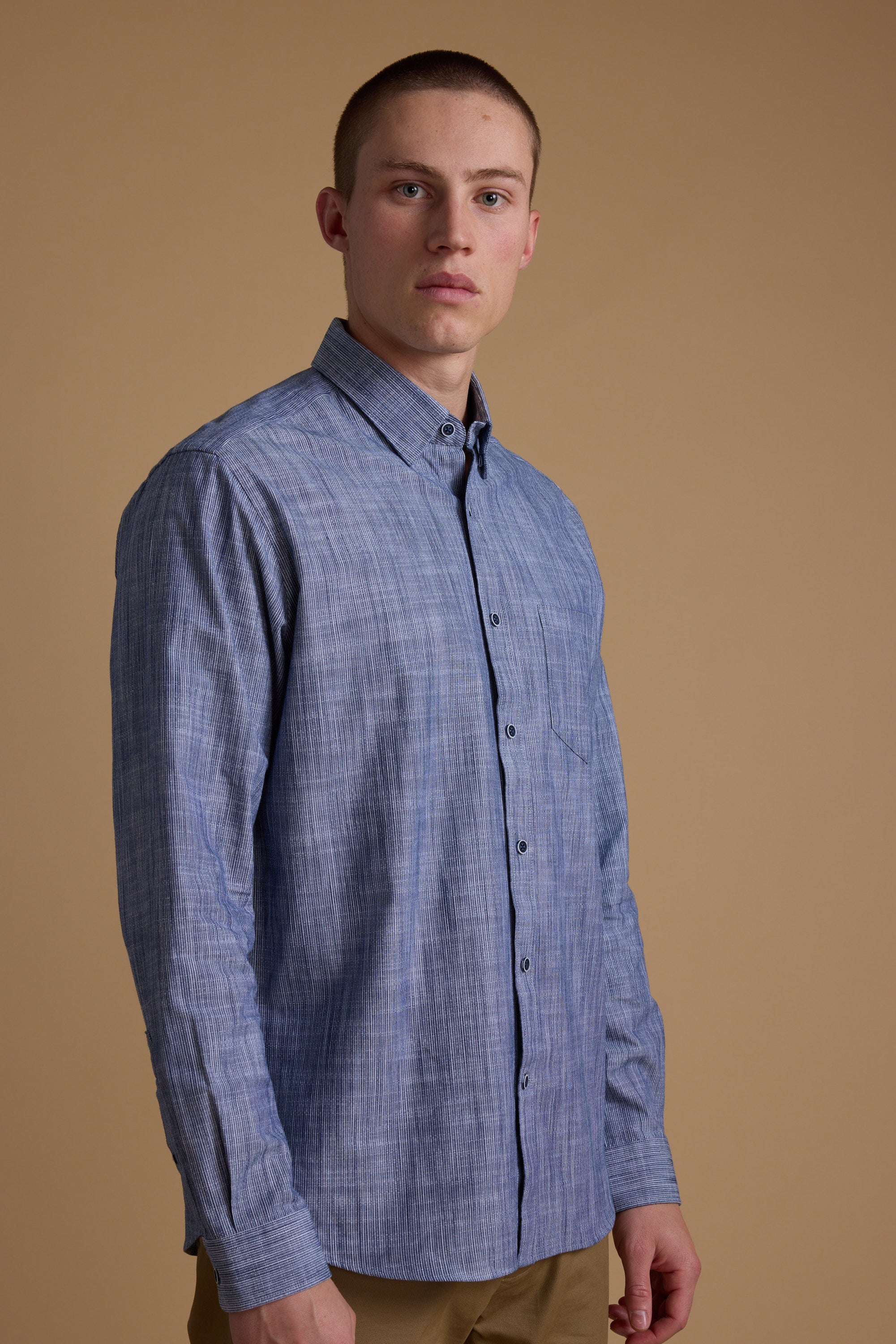 A young man with short hair wears the Barkers Blaine Stripe Shirt and beige pants, standing against a plain beige background and looking slightly to the side.
