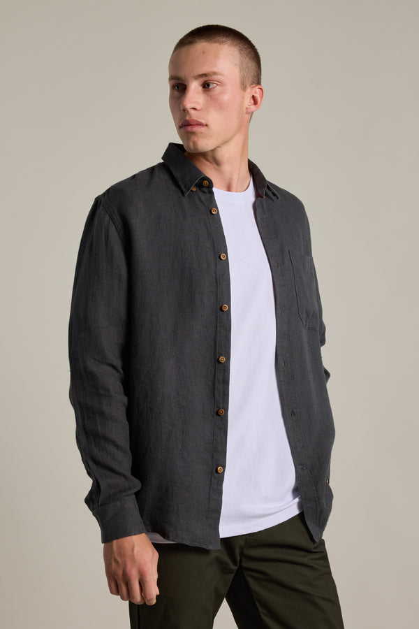 A person wearing the Barkers Delano Linen Shirt in a classic dark shade over a white tee and dark pants stands slightly sideways, looking left against a plain light background.