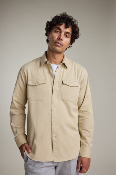 A man with curly dark hair wears the Barkers Chadwick Overshirt—a heavyweight cotton layer—over a white T-shirt and light gray pants, standing against a plain light background with a neutral expression.