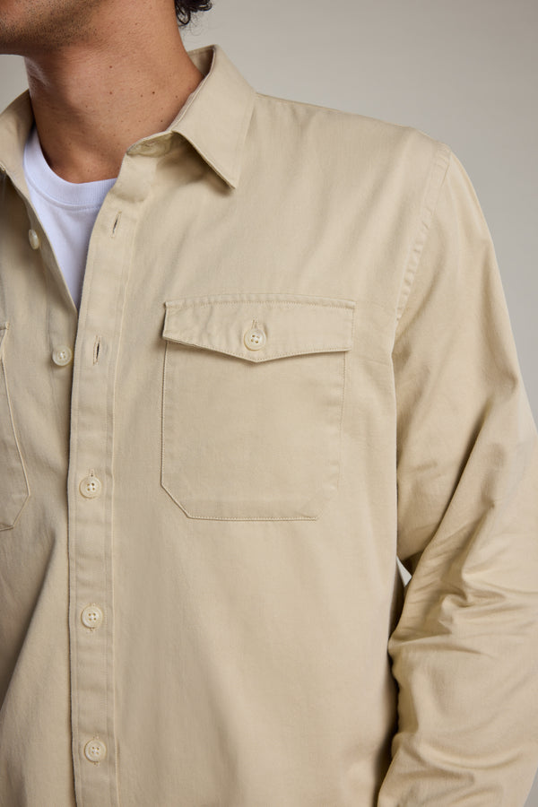 A person wears the Barkers Chadwick Overshirt in beige heavyweight cotton over a white tee. The overshirt features a buttoned chest pocket, with only the upper torso and part of the face visible, highlighting this versatile layering piece.