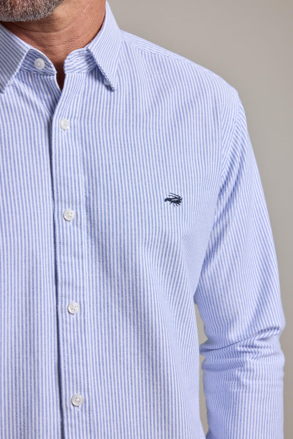 A man wears the Barkers Maynard Oxford Stripe Shirt, featuring light blue and white vertical stripes, responsibly sourced cotton, and a small chest logo. The image shows the men's classic shirt from shoulders to waist.