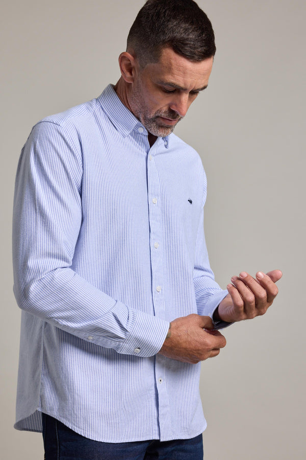 A man with short dark hair and a trimmed beard wears the Barkers Maynard Oxford Stripe Shirt in a classic fit, made from responsibly sourced cotton. He looks down while adjusting his cuff against a plain background.