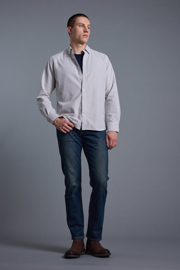 A person stands against a gray background, wearing the Barkers Maynard Oxford Stripe Shirt with dark blue jeans and brown shoes. They have short hair and look slightly to the side, one hand on their hip.