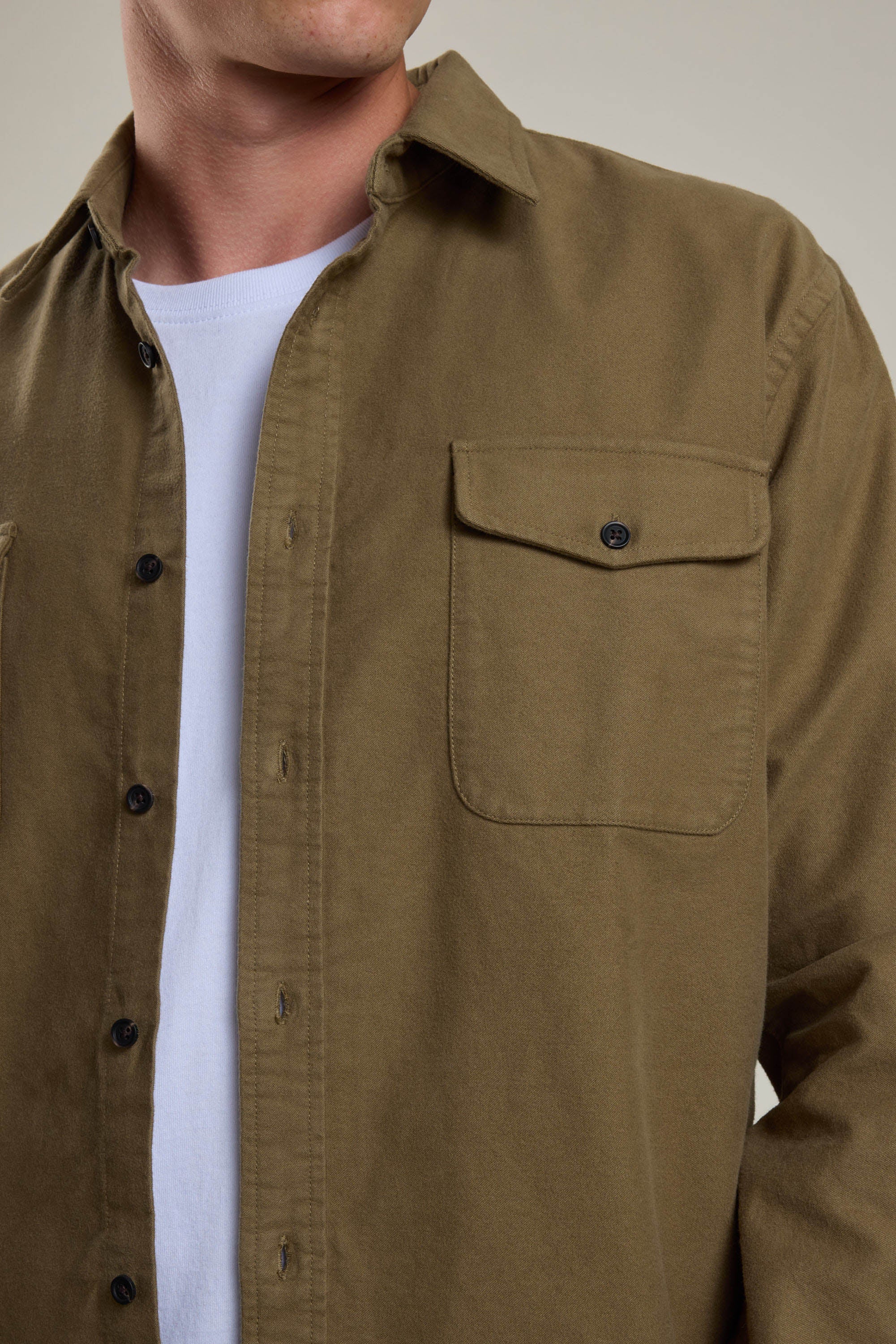 A person wears the Barkers Tayler Moleskin Overshirt in olive green, crafted from responsibly sourced cotton with a buttoned chest pocket and black buttons, over a white t-shirt. The person's head is partially out of frame.