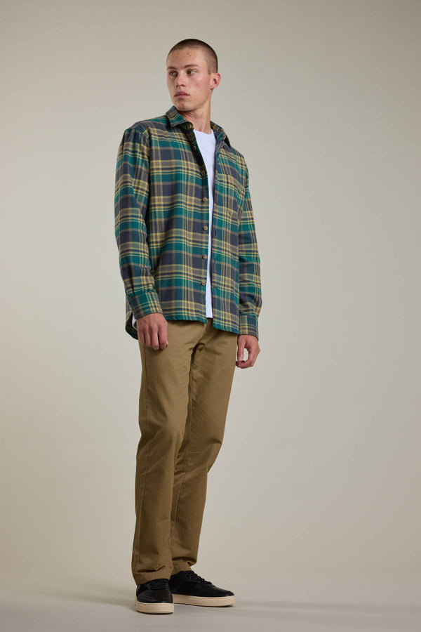 A young man models the Barkers Wallis Check Overshirt, layered over a white tee with tan chinos and black sneakers. He looks to the side, highlighting this versatile men’s wardrobe essential against a simple background.