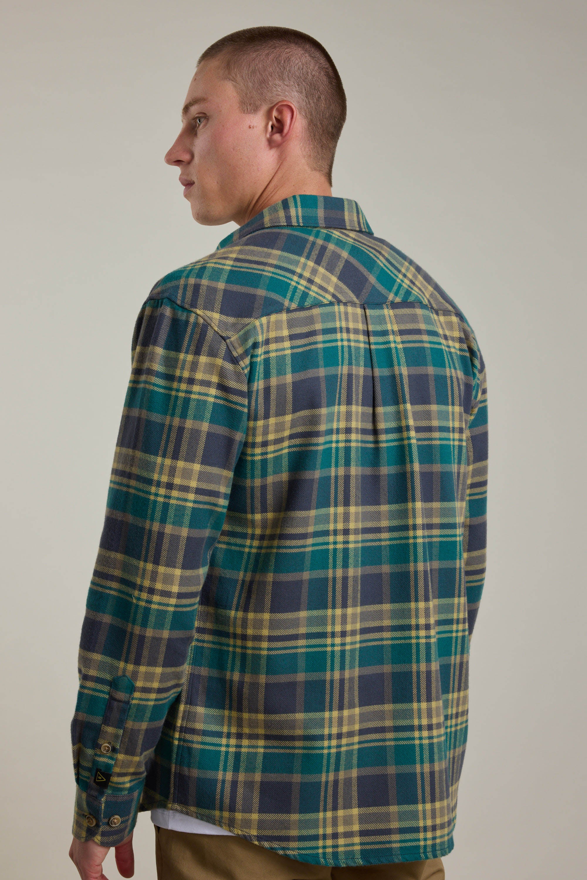 A man with short hair, seen from behind and looking left, wears the Barkers Wallis Check Overshirt in green, yellow, and blue—an essential addition to any men's wardrobe. He stands against a plain light background.