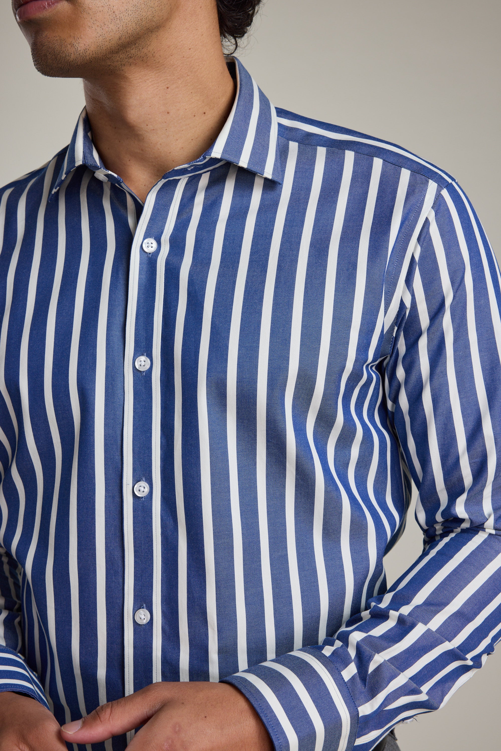 A person wears the Barkers Nandas Stripe Business Shirt, featuring blue and white vertical stripes, a tailored fit, and wrinkle-resistant fabric; one hand is near the waist and their face is partially out of frame.