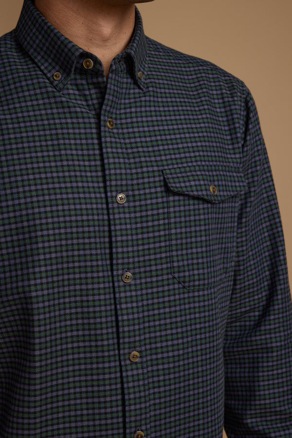 Model wears the Barkers Starle Check Shirt in blue and green check, featuring a buttoned collar and front pocket. Crafted from responsibly sourced cotton, the vintage-style shirt is shown against a plain beige background, focusing on the upper torso.