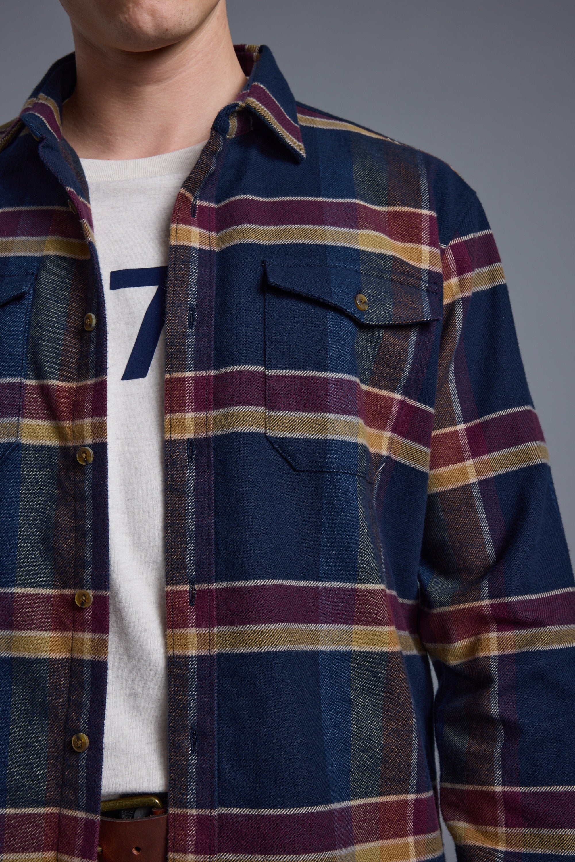 A person wears the Barkers Heaton Check Overshirt, made from responsibly sourced cotton, over a white T-shirt with a partial number 7 visible. The image is cropped at the shoulders and waist.