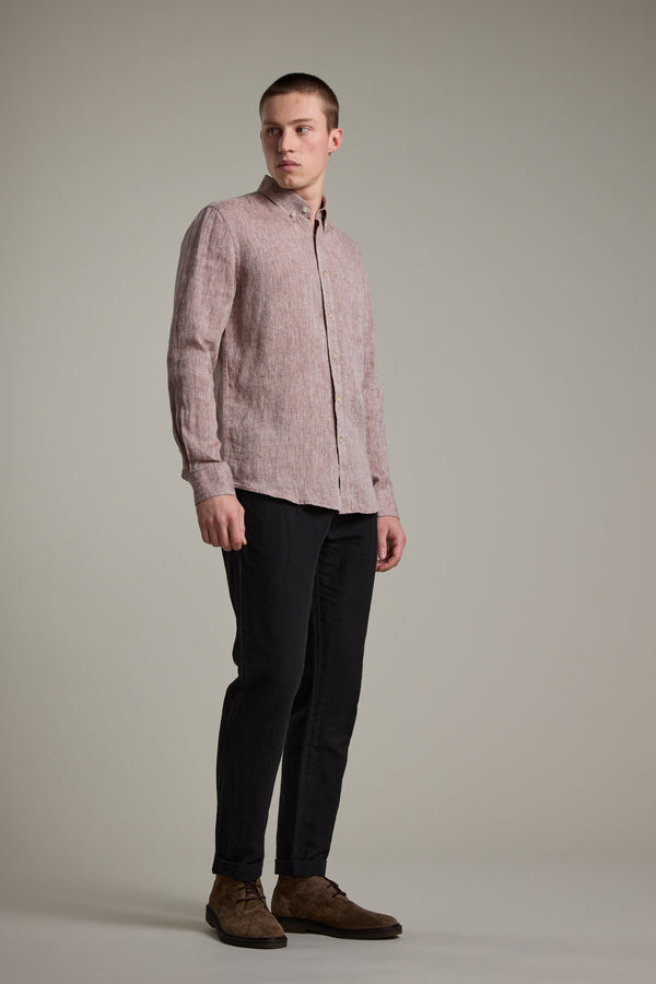 A man stands against a plain background wearing the Barkers Dorset Linen Shirt in light pink, featuring a tailored fit, paired with dark pants and brown shoes, gazing slightly to his left.