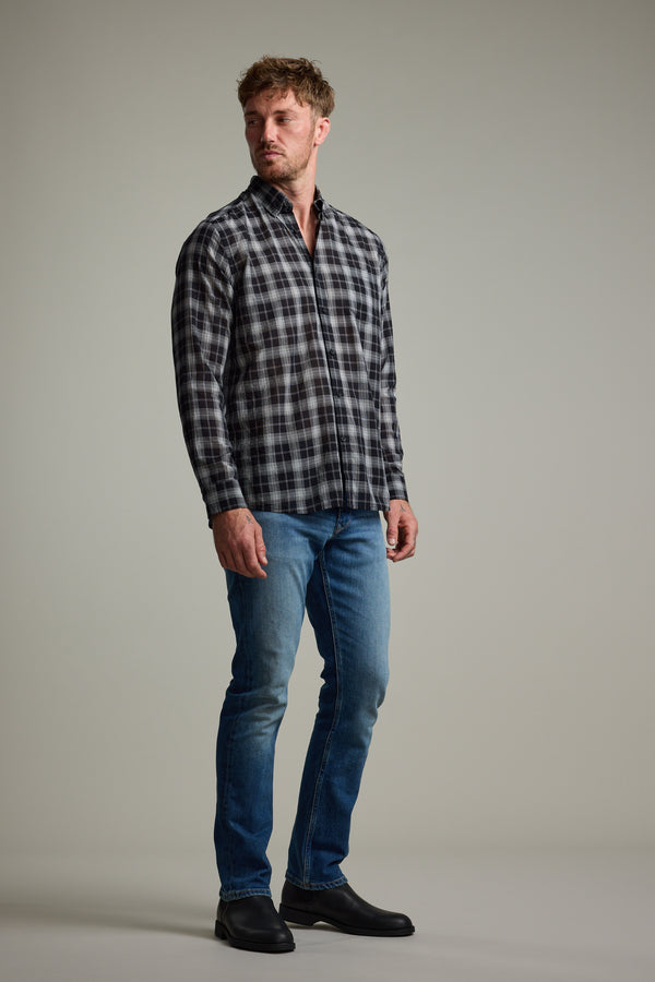 A man stands facing slightly left, wearing the Barkers Carter Check Shirt in black and white, paired with blue jeans and black boots, set against a plain light gray background.