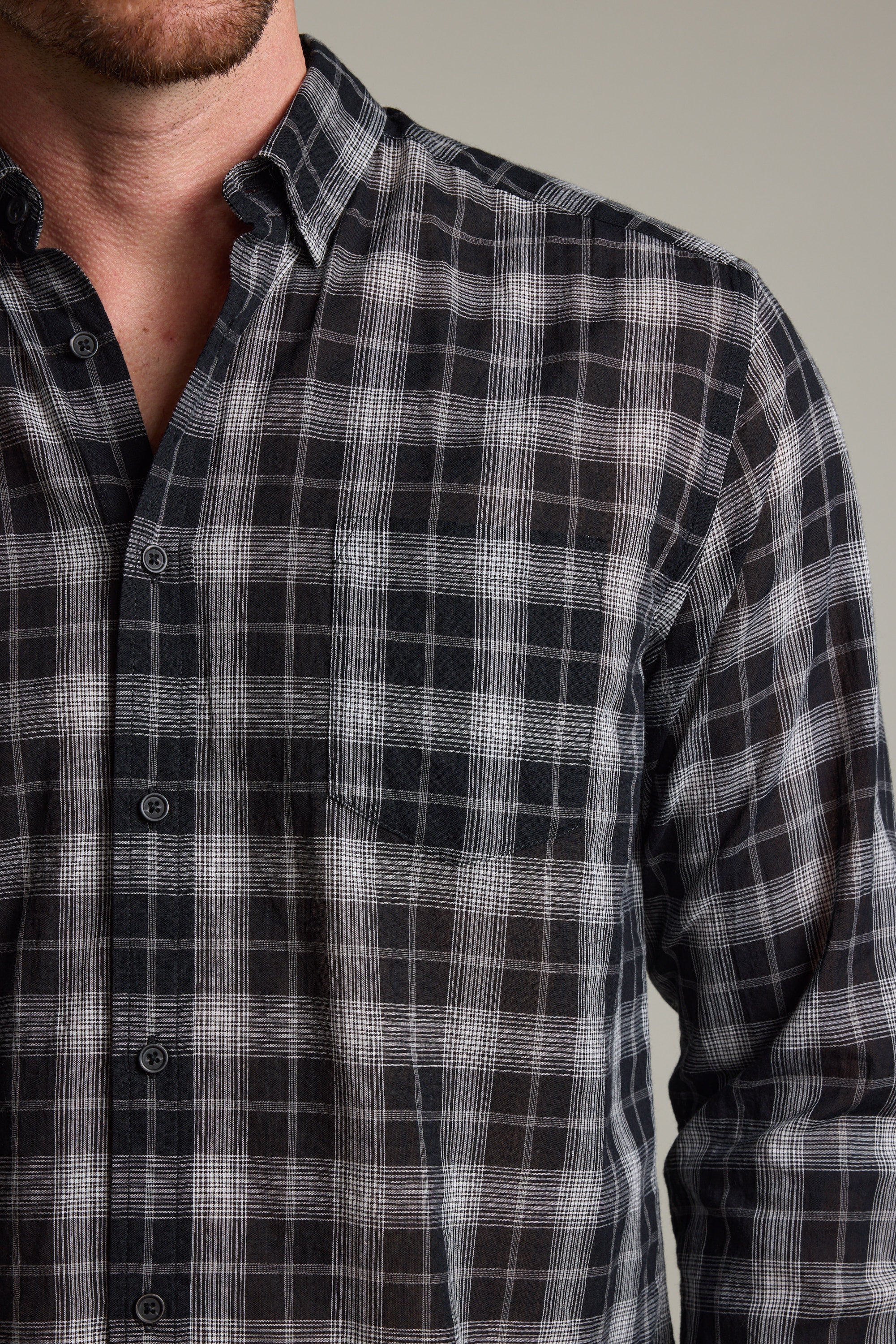 A person is shown from shoulders to mid-torso wearing the Barkers Carter Check Shirt, a lightweight long-sleeve shirt featuring a black and white plaid pattern, with part of the face visible against a neutral background.