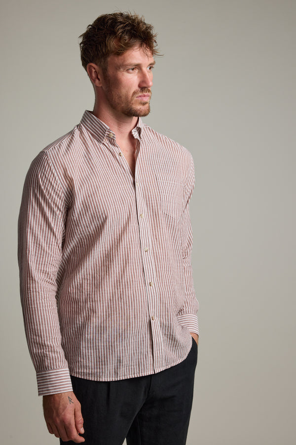 A man with short, tousled hair models the Barkers Sumter Stripe Shirt—a lightweight, red and white striped button-up—paired with dark pants, standing slightly left against a plain light gray background.