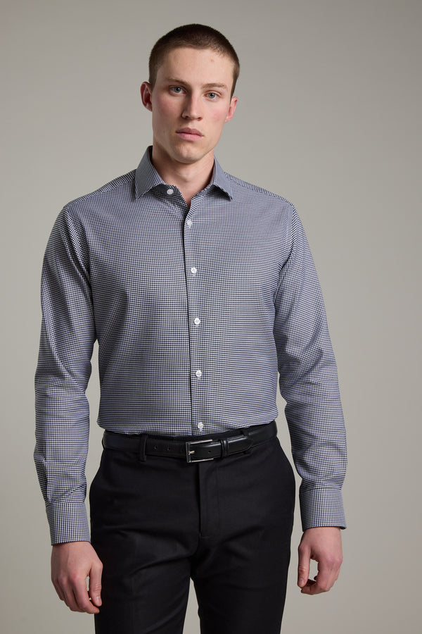 A young man with short hair models the Barkers Mitchel Check Business Shirt with black pants against a plain light gray background, looking directly at the camera with a neutral expression.