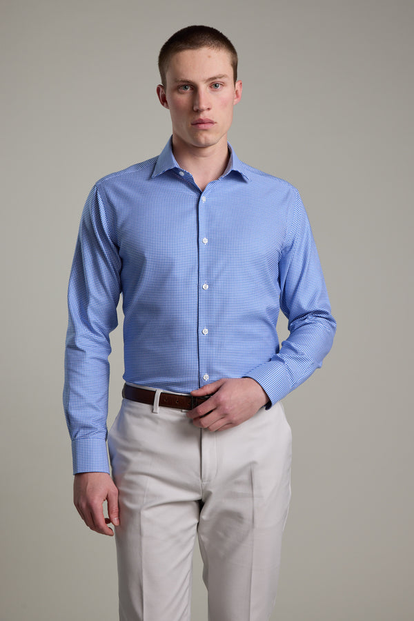 A man wearing the Barkers Mitchel Check Business Shirt, tailored fit with a light blue check pattern, is seen tucked into beige trousers with a brown belt, standing against a plain background and looking directly at the camera.