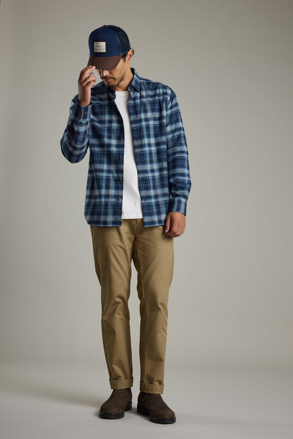Man in Barkers Lexington Check Shirt, khaki pants, and cap, looking down touching his hat.