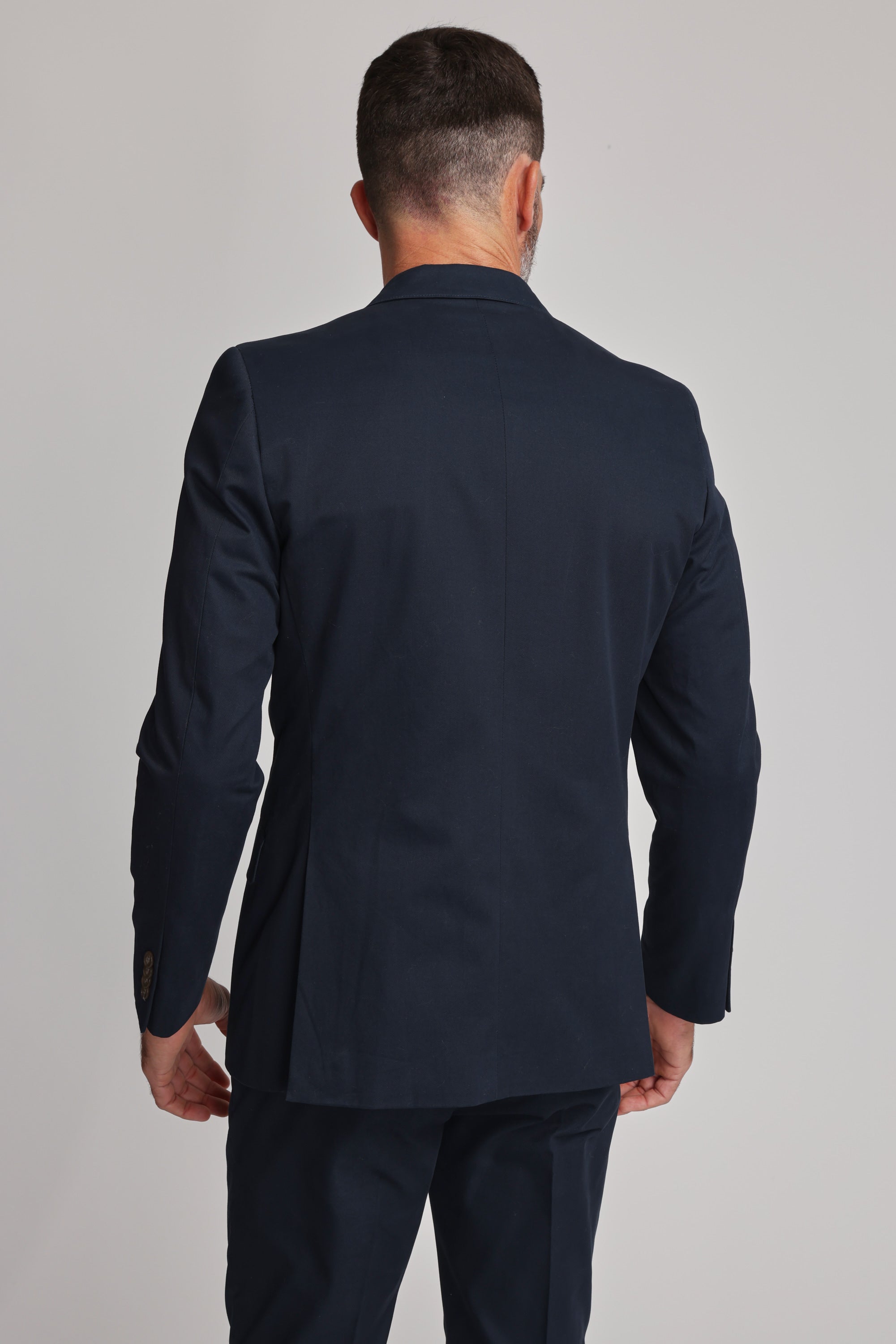 A man wearing a dark navy Barkers Maclay Twill Blazer stands facing away from the camera, arms relaxed by his sides, against a plain light background.