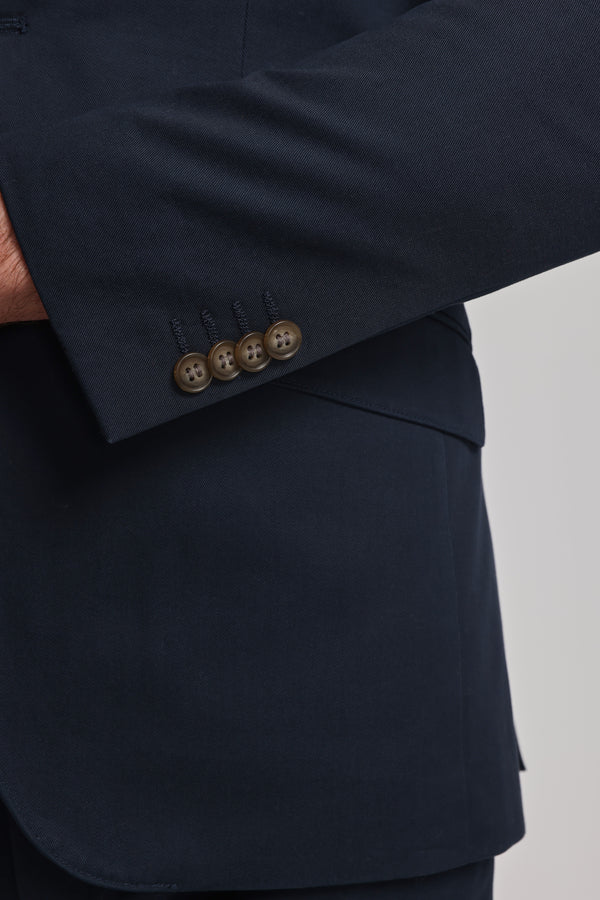 Close-up of a person wearing the Barkers Maclay Twill Blazer, highlighting its dark navy sleeve with four brown buttons near the cuff against a plain, light-colored background.