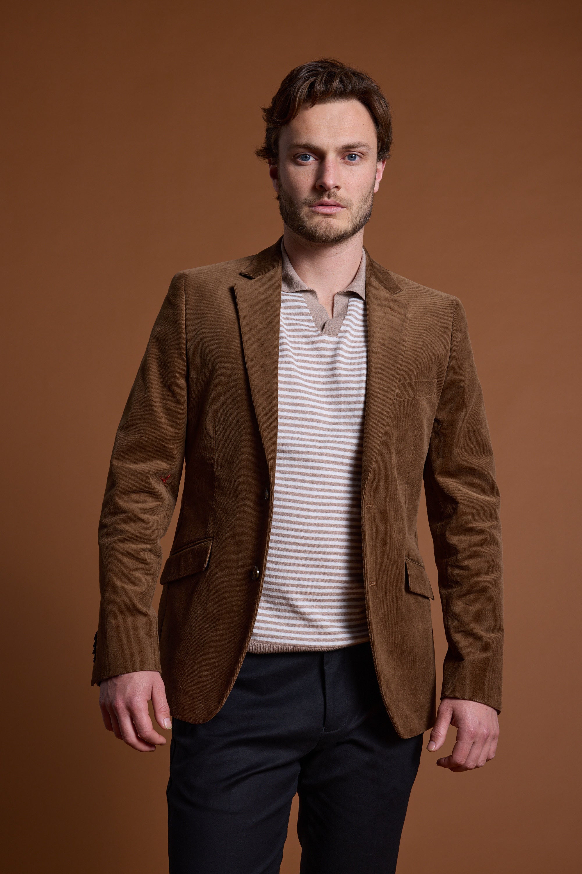 A man with light brown hair and a beard wears the Barkers Parkway Cotton Stripe Polo under a brown blazer with dark pants, standing against a plain brown background.