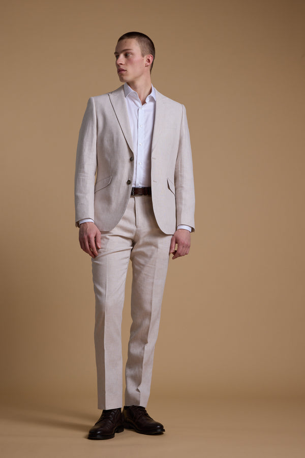 A man stands against a plain beige background, wearing the Barkers Somerton Texture Pant, paired with a white dress shirt and dark brown shoes. He looks to the side, one hand resting on his trouser.