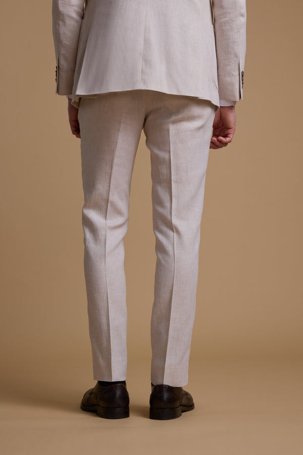 A person stands facing away from the camera, wearing Barkers Somerton Texture Pant in light beige and dark brown dress shoes, set against a plain light brown background.