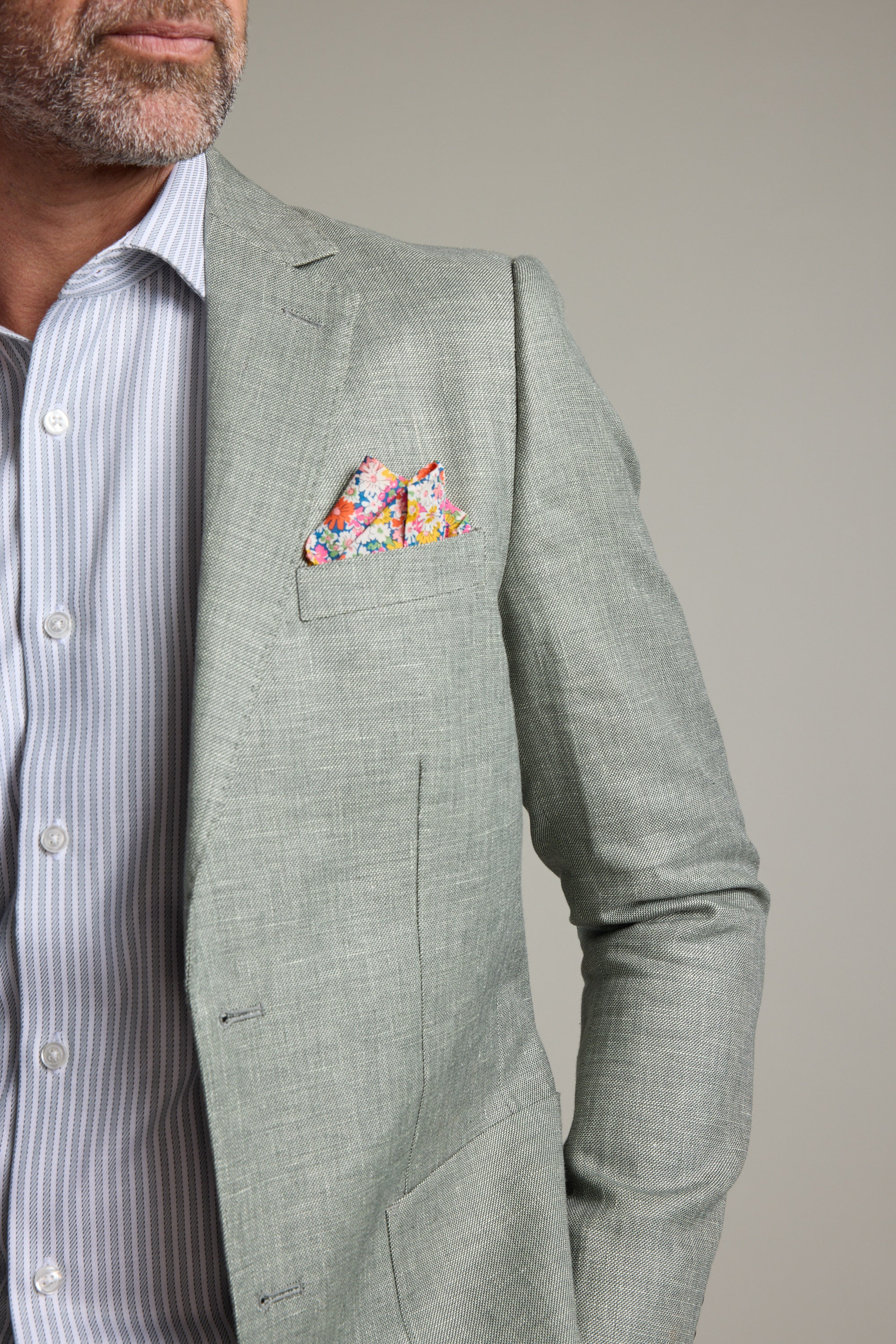 A man wears the Barkers Marion Texture Blazer with a floral pocket square and light blue striped shirt, shown from shoulders to waist against a plain background—a stylish choice for summer occasions.
