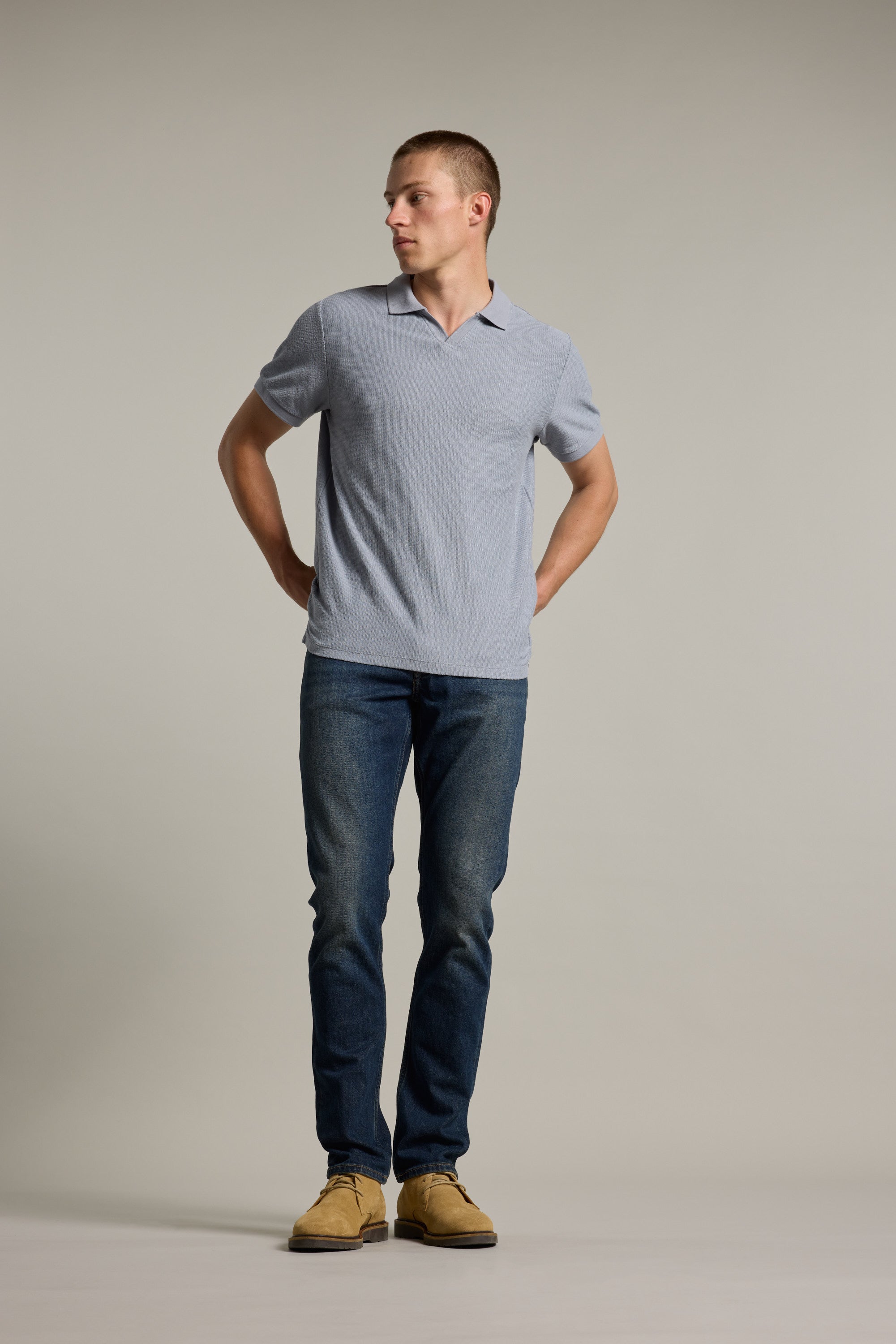 Man in a Barkers Winfield Textured Polo, jeans, and tan shoes stands against a plain background.