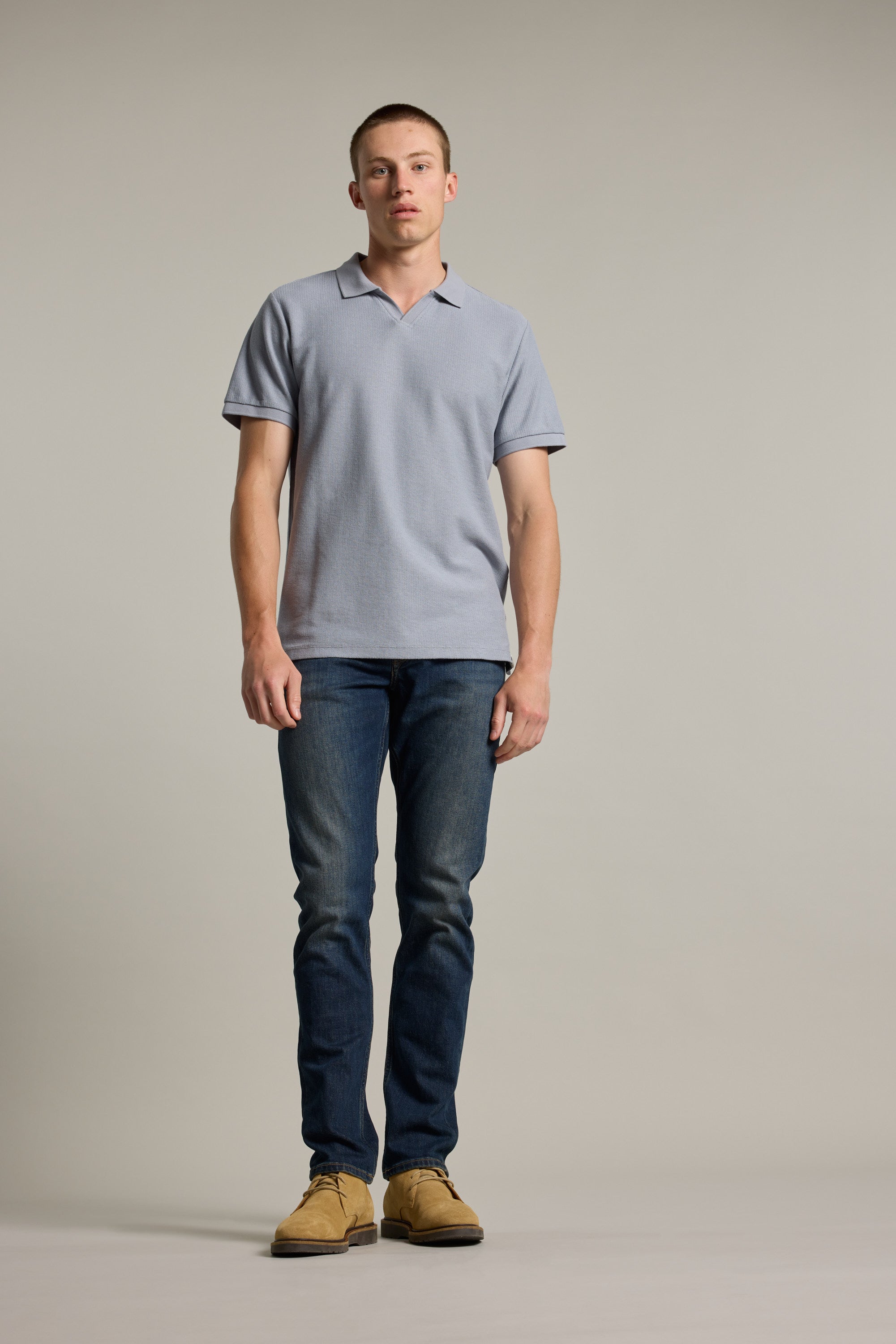 A man in a Barkers Winfield Textured Polo, jeans, and tan shoes stands against a plain background.