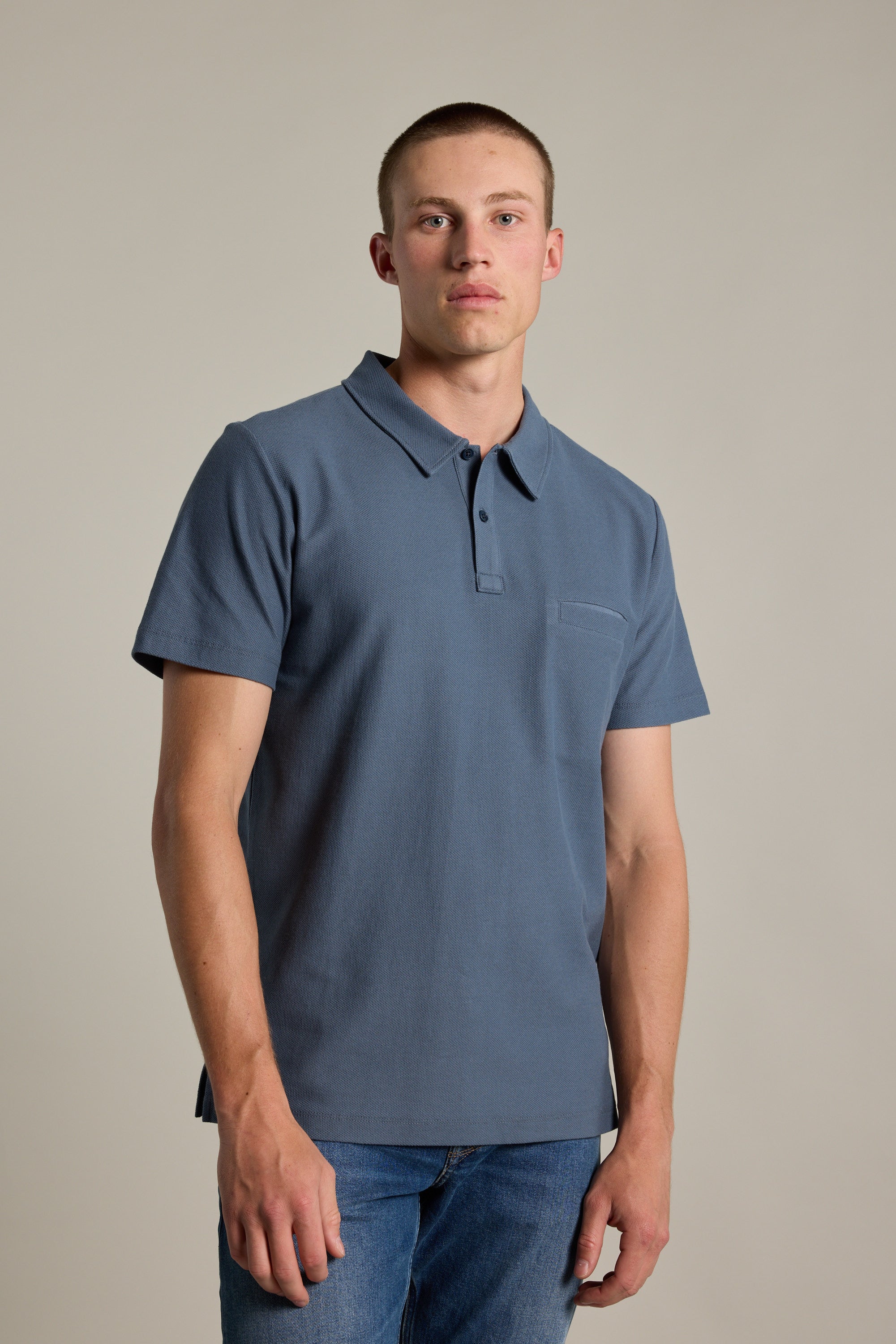 A young man with short hair stands against a plain background, wearing Barkers' Canal Polo and blue jeans, looking directly at the camera with a neutral expression.