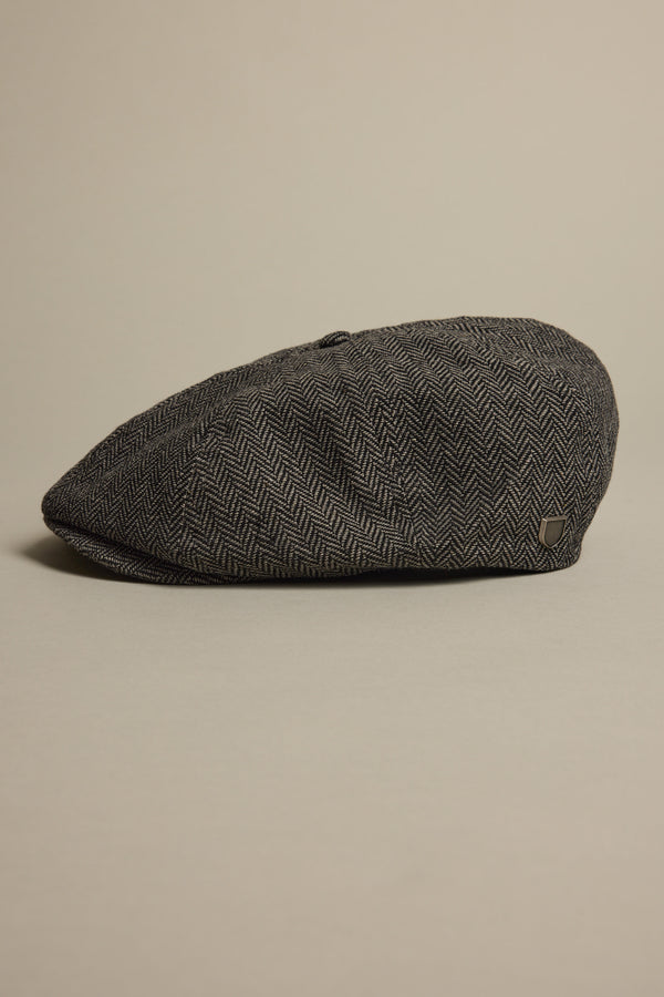 The Brixton Brood Snap Cap by Brixton rests on a light surface, displaying its gray herringbone wool-blend fabric, side profile, and textured pattern.