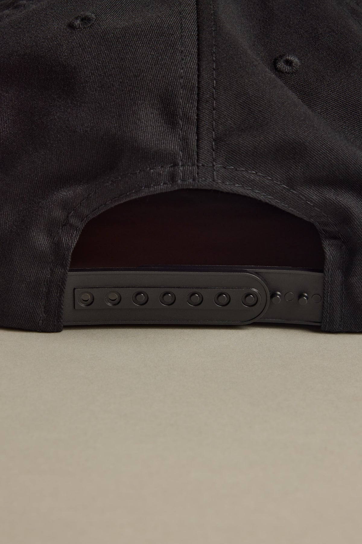 Close-up of the Brixton Payment MP Snapback’s adjustable back on a beige surface.