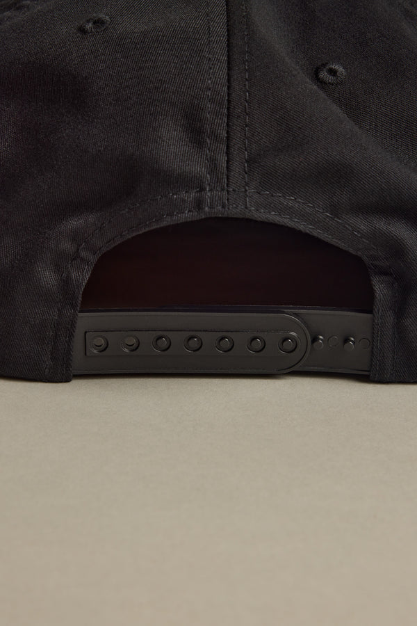Close-up of the Brixton Payment MP Snapback’s adjustable back on a beige surface.
